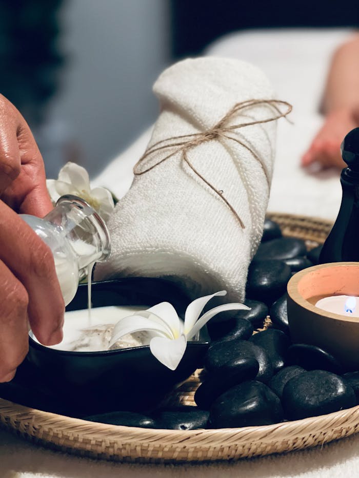 digital Hand pouring oil in spa setting with stones, towel, and calming ambiance.