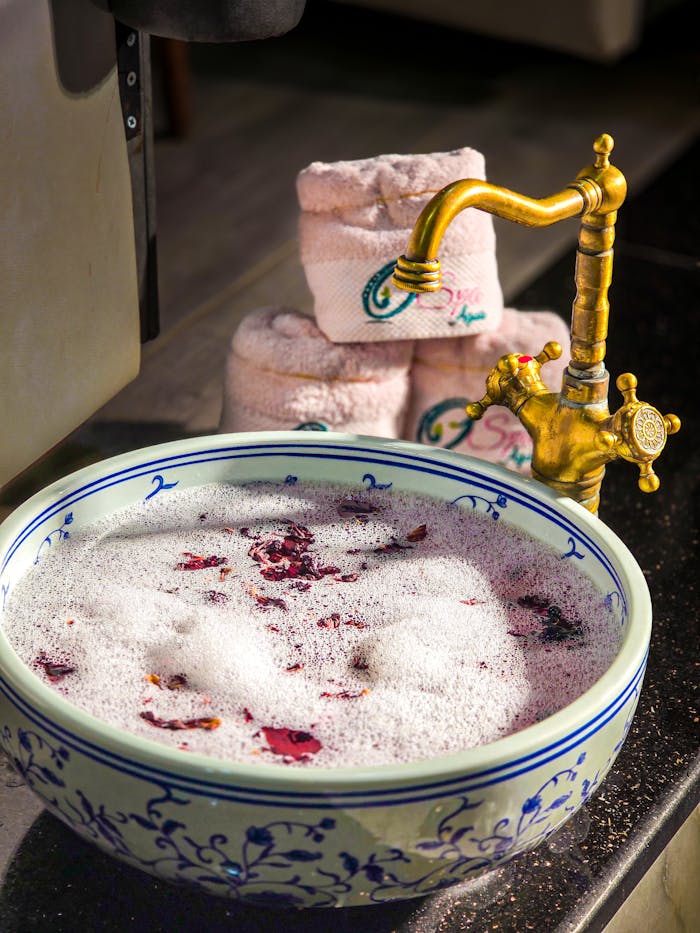 digital-01 A luxurious spa bowl with rose petals and foam, accompanied by rolled towels and a vintage faucet.